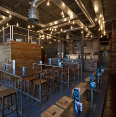 an empty restaurant with wooden tables and stools in front of brick walls, exposed beams and industrial lighting