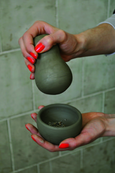 a woman is pouring something out of a clay pot into a bowl in front of a tiled wall