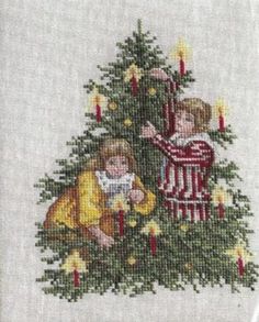 a cross stitch christmas tree with two children on it and lit candles in the background