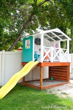 a small play house with a slide in the grass next to a white picket fence