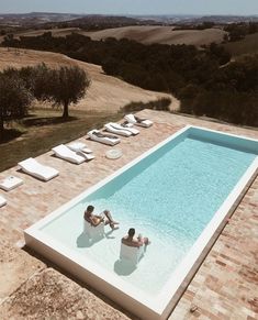 two people lounging on lounge chairs next to an outdoor swimming pool in the countryside