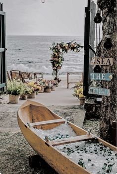 a wooden boat filled with lots of bottles next to the ocean and flowers in vases