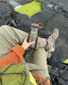 a person sitting on the ground holding a water bottle in their hand and looking down at them