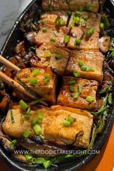 tofu in a pan with chopsticks on the side and green onion garnish