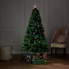 a lit christmas tree with presents under it on the floor in front of a chair