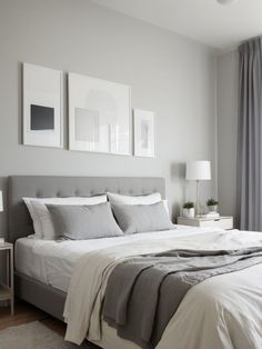 a bedroom with white and gray bedding, two pictures on the wall above the bed