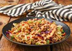 a plate full of noodles and vegetables on a wooden table next to a striped napkin