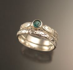 two silver rings with a green stone in the center and leaves on each side, sitting on a black surface