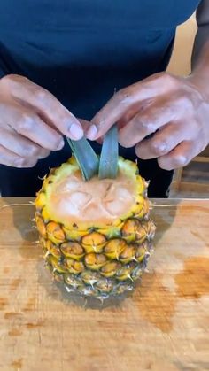 a person cutting up a pineapple on top of a wooden table with a knife