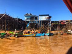 several small boats floating on top of a river next to wooden huts and shacks