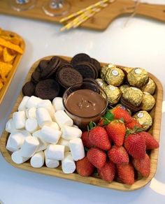 a tray filled with marshmallows, chocolate and strawberries next to other snacks