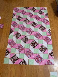 a pink and green patchwork quilt sitting on top of a wooden floor