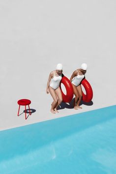 two women in white bathing suits standing next to a pool with a red life preserver