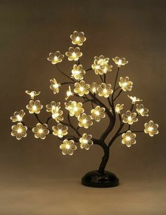 a lighted tree with white flowers in the shape of leaves on a black stand against a gray background