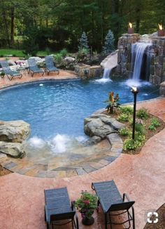 a backyard with a pool and waterfall in the middle, surrounded by lawn chairs on either side