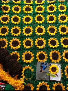 a crocheted blanket with sunflowers on it next to yarn and scissors