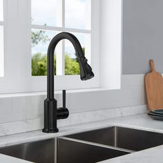 a kitchen sink with a black faucet next to a window and cutting board