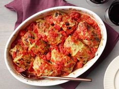 a casserole dish with tomatoes and onions in it on a table next to wine glasses