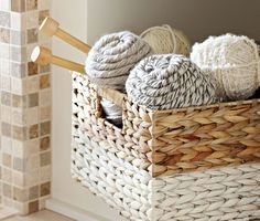 a basket filled with balls of yarn next to a brick wall and wooden spoons