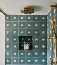 a green tiled shower with gold fixtures and white starburst tiles on the wall