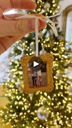 someone is holding up a photo ornament in front of a christmas tree