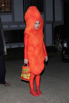 a woman in an orange costume is walking down the street with her handbag on her hip