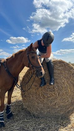 a woman riding on the back of a brown horse next to a hay bale