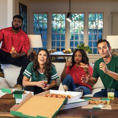 four people sitting on a couch eating pizza