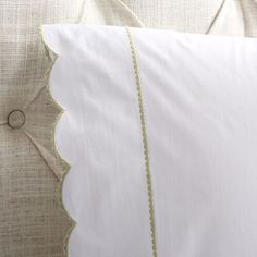 a close up of a pillow on a bed with white linens and green trim