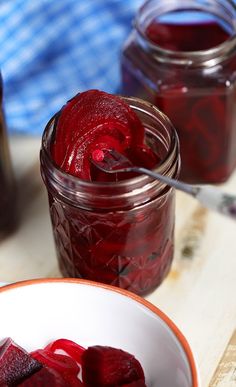 two jars filled with pickled beets on top of a wooden table next to a spoon