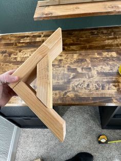 a person holding a piece of wood in front of a wooden table with other items on it