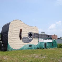 an old building with a giant guitar painted on it's side in the grass