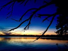 the sun is setting over a lake with trees in front of it and some water