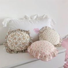 three pillows are sitting on top of a white dresser next to a pillow with a heart