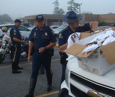 two police officers standing next to a white car with boxes on the hood and in front of them