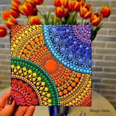 a hand holding up a colorful card with flowers in the background and a vase full of tulips behind it