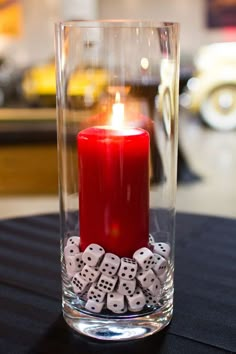 a red candle is sitting in a glass vase with dice around it on a table