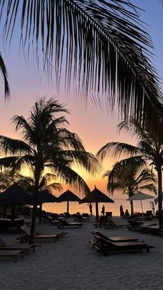 the sun is setting on the beach with lounge chairs and umbrellas