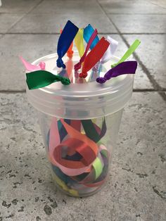 a plastic cup filled with colorful streamers on top of a tiled floor next to a wall