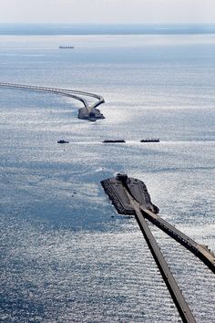 an aerial view of a bridge spanning over the ocean with ships in the water behind it