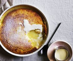 a baked dessert in a white dish next to a cup of milk and a spoon