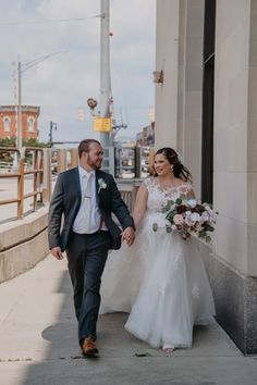 a bride and groom walking down the sidewalk