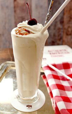 there is a drink with whipped cream and cherries in it on the table next to a checkered cloth