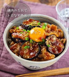 a bowl filled with food next to chopsticks on top of a purple cloth