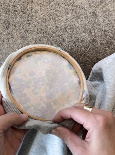 two hands are holding a round object on a cloth with holes in the middle and one hand is stitching it together