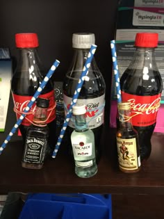 three bottles of soda sit on a shelf next to blue bins with straws in them