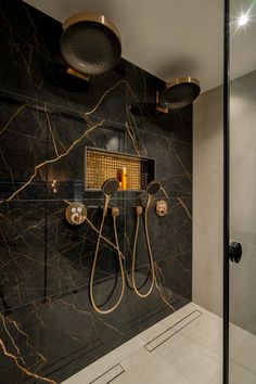 a bathroom with black marble and gold fixtures on the wall, along with an overhead shower head