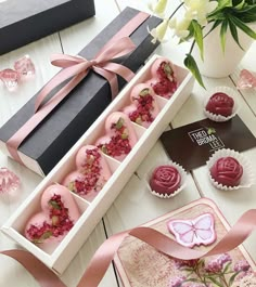 a box filled with lots of pink cupcakes next to a bouquet of flowers