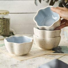 a person is holding their hand over four bowls on top of a table with papers