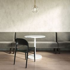 a white table and two black chairs in a room with concrete walls, wood flooring and a light bulb hanging from the ceiling